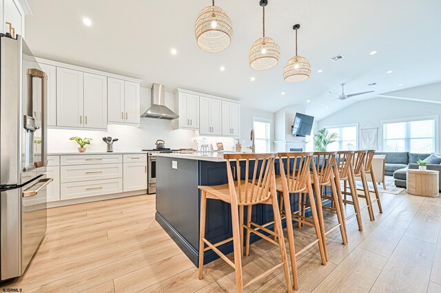 kitchen featuring wall chimney range hood, white cabinetry, lofted ceiling, light wood-type flooring, and premium appliances