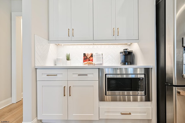 bar with baseboards, light wood finished floors, appliances with stainless steel finishes, and tasteful backsplash