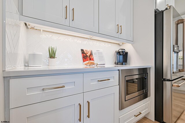 bar with tasteful backsplash, stainless steel appliances, and light wood-style flooring