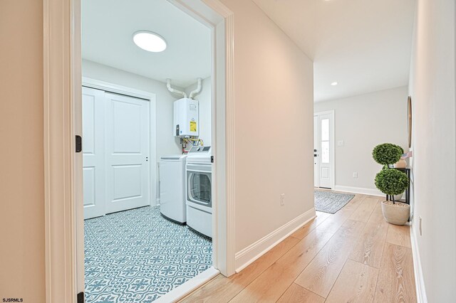 washroom featuring laundry area, baseboards, tankless water heater, light wood finished floors, and washer and clothes dryer