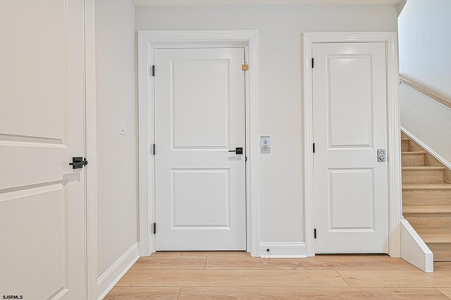 hallway featuring stairs, baseboards, and light wood-type flooring