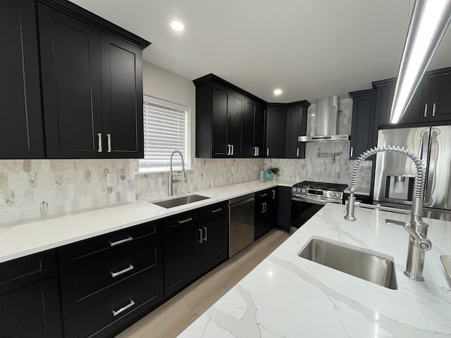 kitchen with wall chimney range hood, dark cabinetry, stainless steel appliances, and a sink