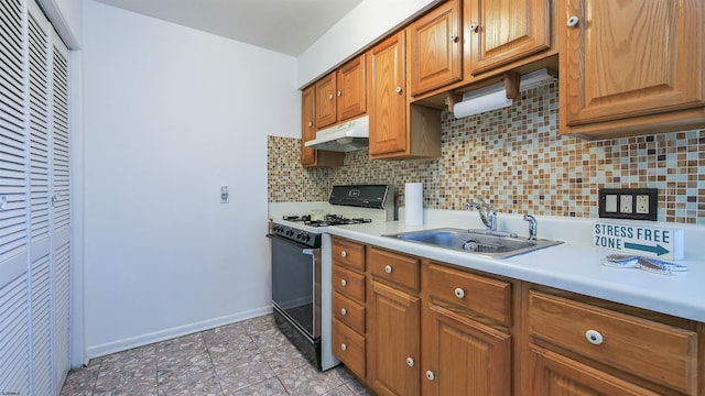 kitchen with a sink, light countertops, gas range, tasteful backsplash, and under cabinet range hood