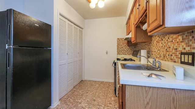 kitchen with brown cabinets, a sink, range with gas stovetop, freestanding refrigerator, and backsplash
