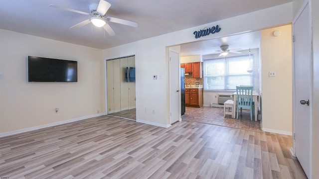 unfurnished bedroom featuring a closet, baseboards, ceiling fan, baseboard heating, and light wood-style flooring