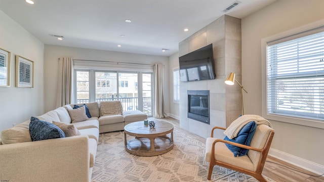 living area featuring light wood-style floors, visible vents, a fireplace, and a wealth of natural light