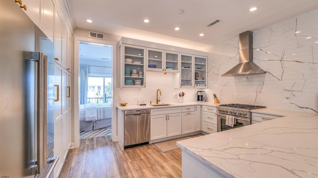 kitchen with wall chimney range hood, high quality appliances, a sink, recessed lighting, and visible vents