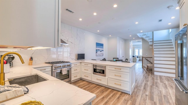 kitchen featuring a peninsula, recessed lighting, white cabinets, a sink, and appliances with stainless steel finishes