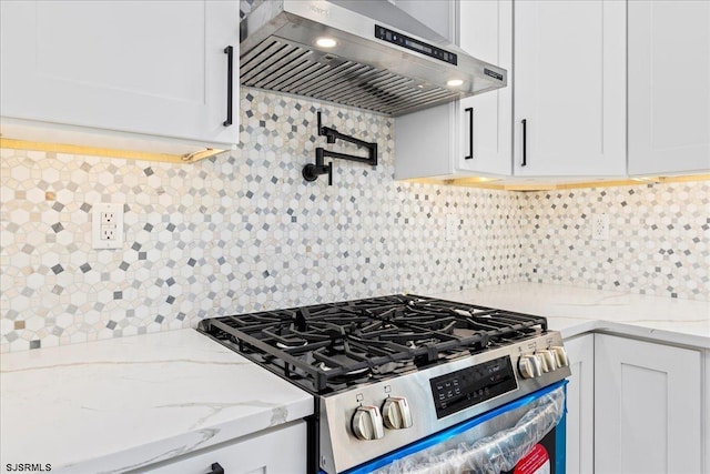 kitchen featuring backsplash, white cabinetry, light stone counters, stainless steel range with gas cooktop, and wall chimney exhaust hood