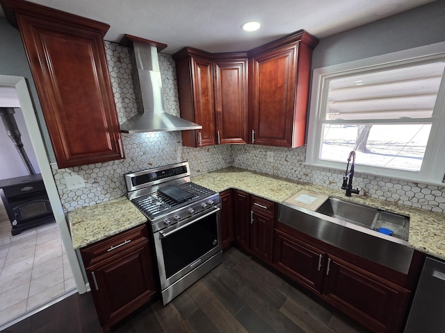kitchen with stainless steel range with gas stovetop, a wood stove, dark brown cabinets, a sink, and wall chimney exhaust hood