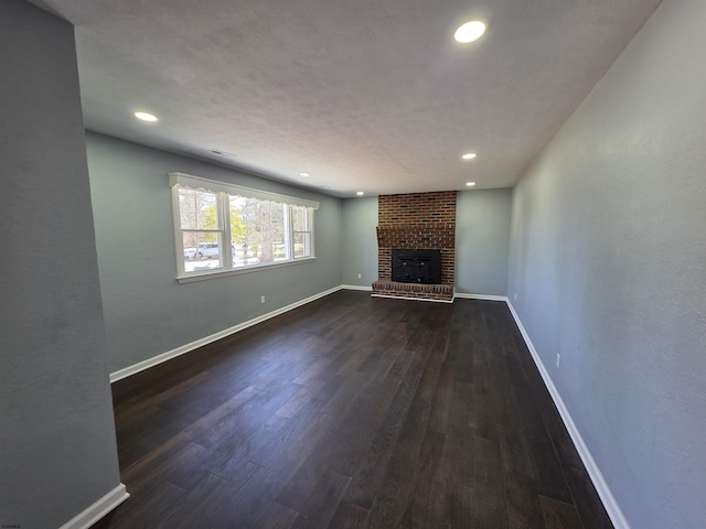 unfurnished living room with a brick fireplace, dark wood-style flooring, baseboards, and recessed lighting