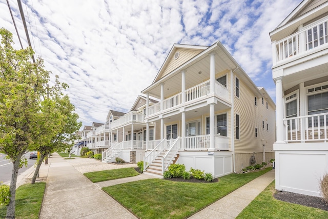 view of front of property featuring a porch, a residential view, a balcony, a front lawn, and stairs