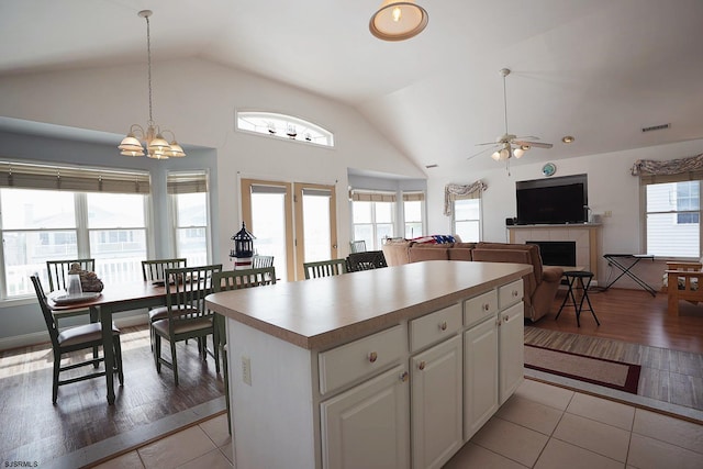 kitchen with white cabinetry, a tile fireplace, ceiling fan with notable chandelier, light tile patterned floors, and vaulted ceiling