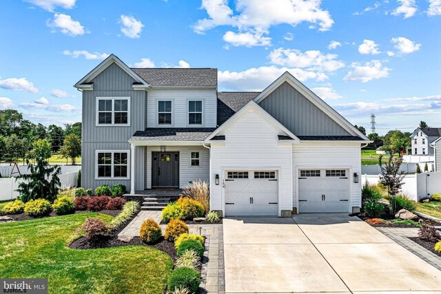 view of front of home with board and batten siding, driveway, roof with shingles, fence, and a front lawn