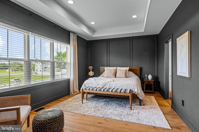 bedroom with recessed lighting, a raised ceiling, light wood finished floors, and visible vents