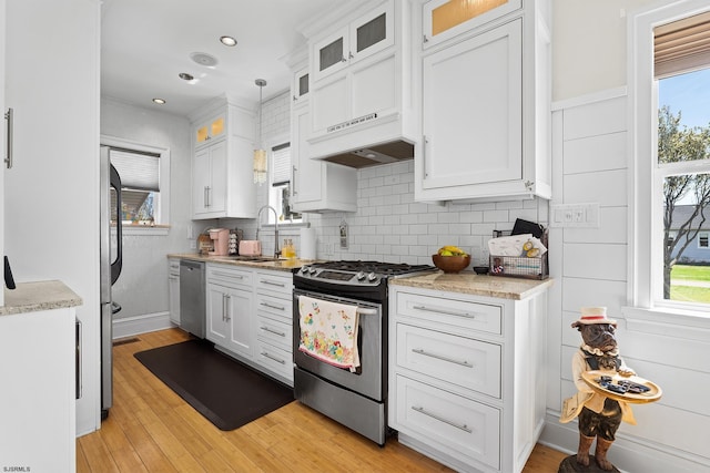 kitchen with light wood finished floors, a sink, decorative backsplash, stainless steel appliances, and white cabinets