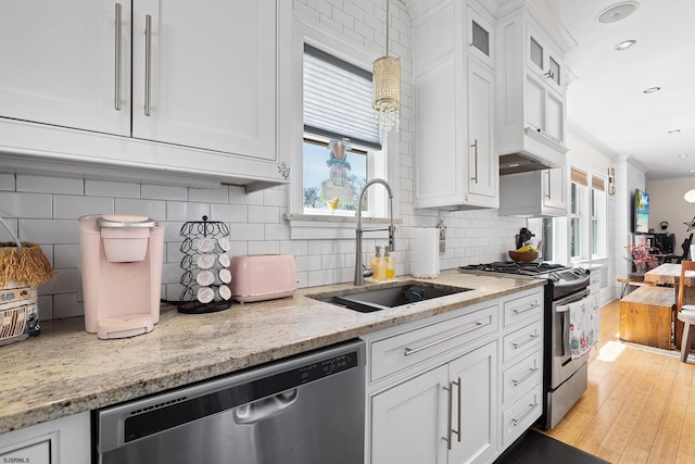kitchen with a sink, stainless steel appliances, tasteful backsplash, light stone counters, and white cabinets