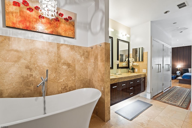 ensuite bathroom with tile walls, visible vents, vanity, a freestanding bath, and connected bathroom