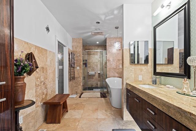 full bath with tile walls, vanity, stone finish floor, a stall shower, and a soaking tub