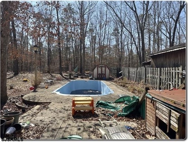 view of pool featuring a storage shed, an empty pool, fence, and an outdoor structure