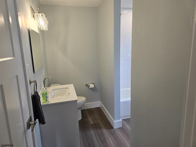 full bathroom with double vanity, toilet, wood finished floors, a sink, and baseboards