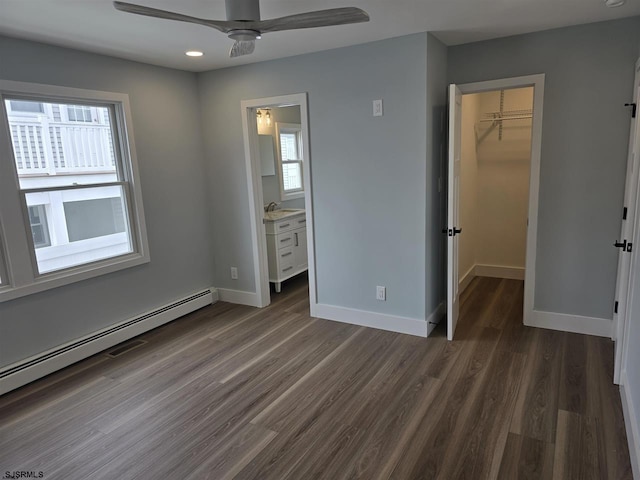 unfurnished bedroom featuring a baseboard radiator, a closet, a walk in closet, baseboards, and dark wood-type flooring