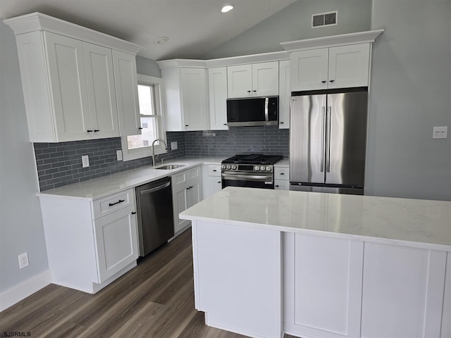 kitchen with a sink, lofted ceiling, stainless steel appliances, visible vents, and decorative backsplash