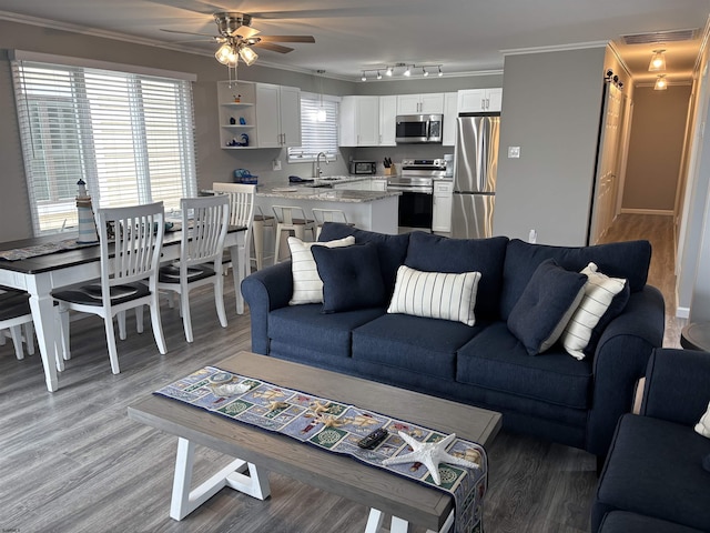 living area with ceiling fan, visible vents, light wood finished floors, and ornamental molding