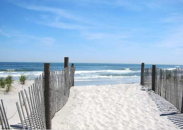 view of home's community featuring a water view, a beach view, and fence