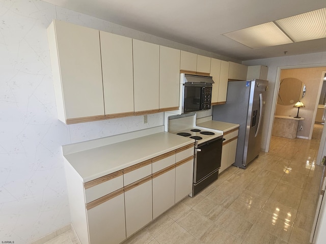 kitchen with range with electric cooktop, black microwave, stainless steel fridge, cream cabinetry, and light countertops