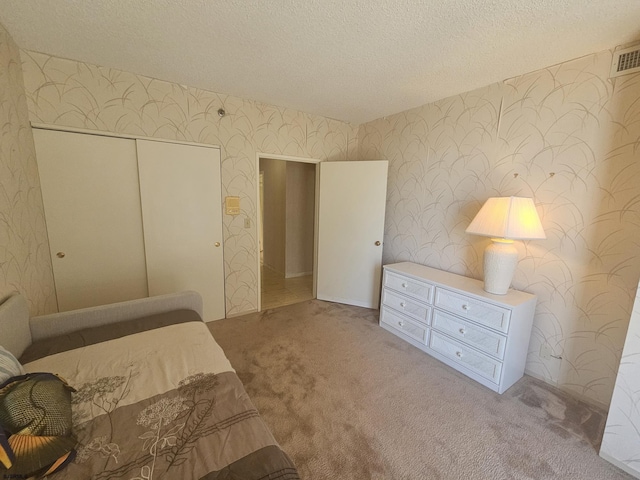bedroom featuring wallpapered walls, carpet flooring, a textured ceiling, and a closet
