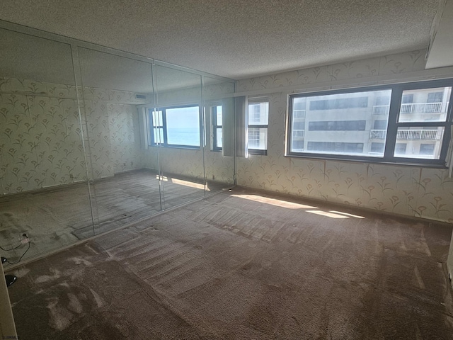 carpeted empty room with wallpapered walls and a textured ceiling