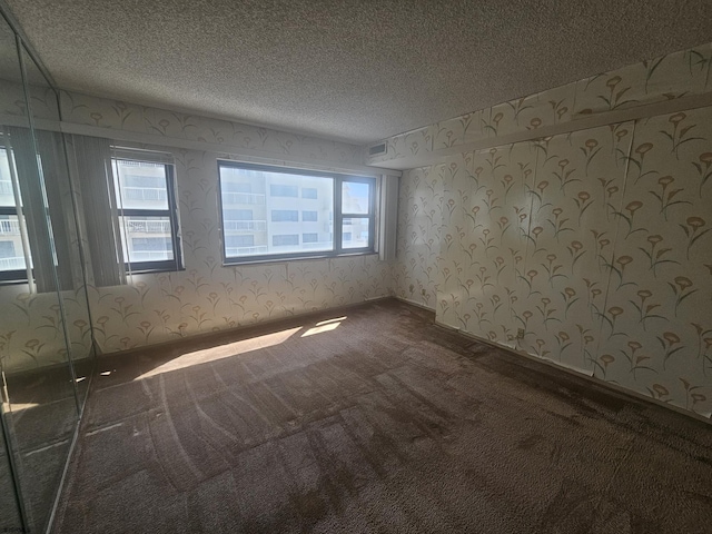 spare room featuring wallpapered walls, carpet, a textured ceiling, and healthy amount of natural light