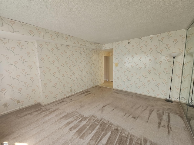 carpeted empty room with wallpapered walls and a textured ceiling