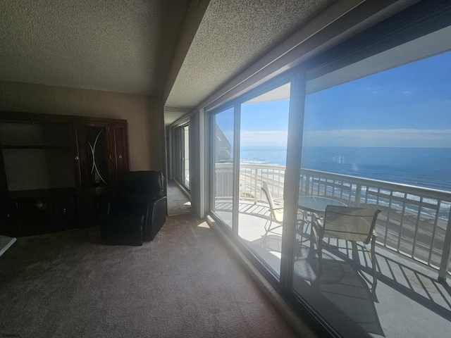 living room featuring view of water and beach, carpet floors, and a textured ceiling