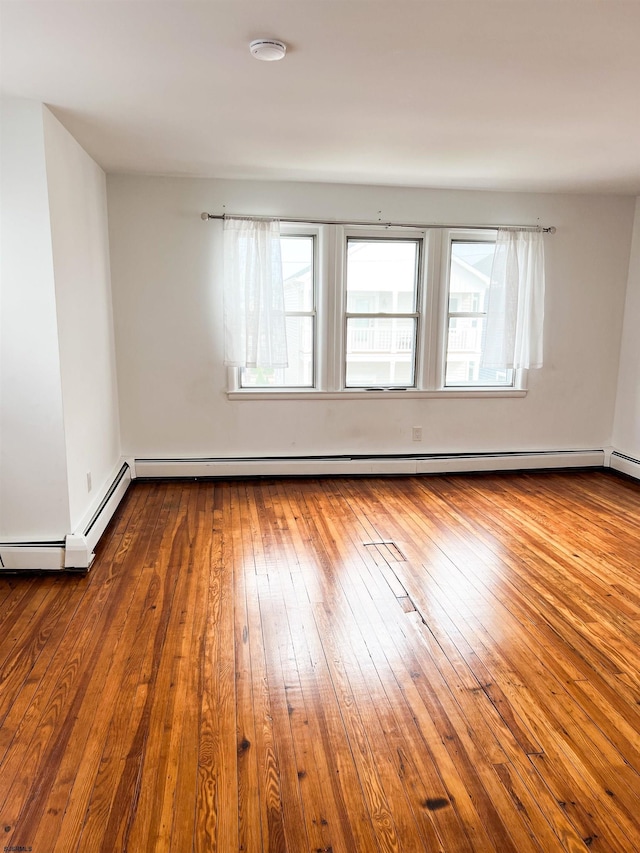 unfurnished room featuring a baseboard heating unit, hardwood / wood-style flooring, and a smoke detector