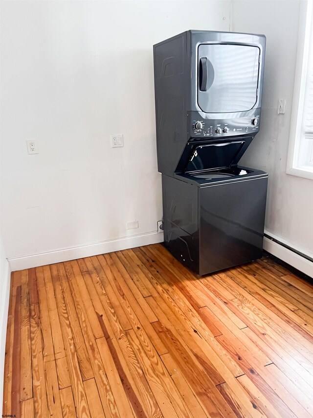 clothes washing area with stacked washer / drying machine, hardwood / wood-style floors, and baseboards