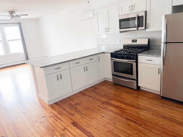 kitchen with appliances with stainless steel finishes, a peninsula, light wood-style flooring, a ceiling fan, and white cabinetry