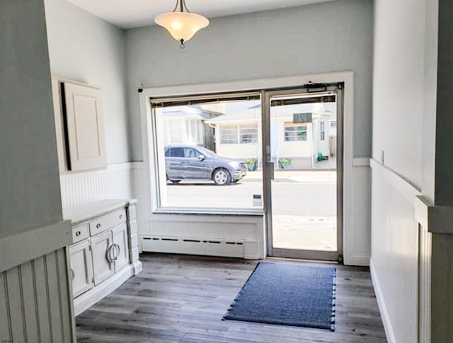doorway to outside with a baseboard heating unit, a wainscoted wall, and wood finished floors
