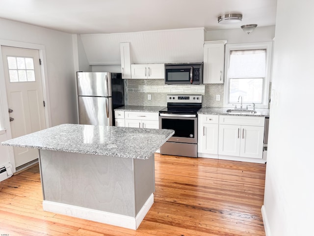 kitchen featuring stainless steel appliances, a sink, backsplash, white cabinets, and light wood finished floors