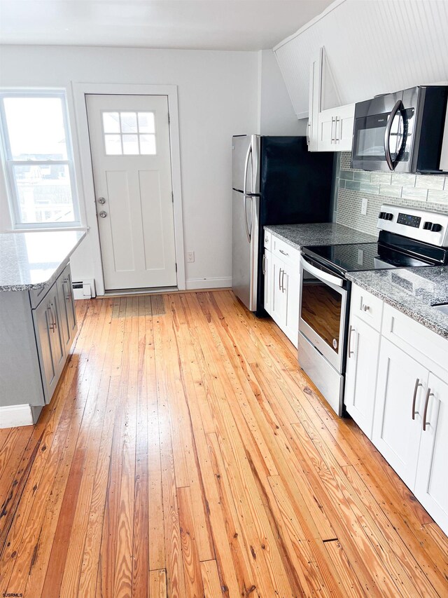 kitchen featuring appliances with stainless steel finishes, a baseboard heating unit, light wood-style flooring, tasteful backsplash, and baseboards