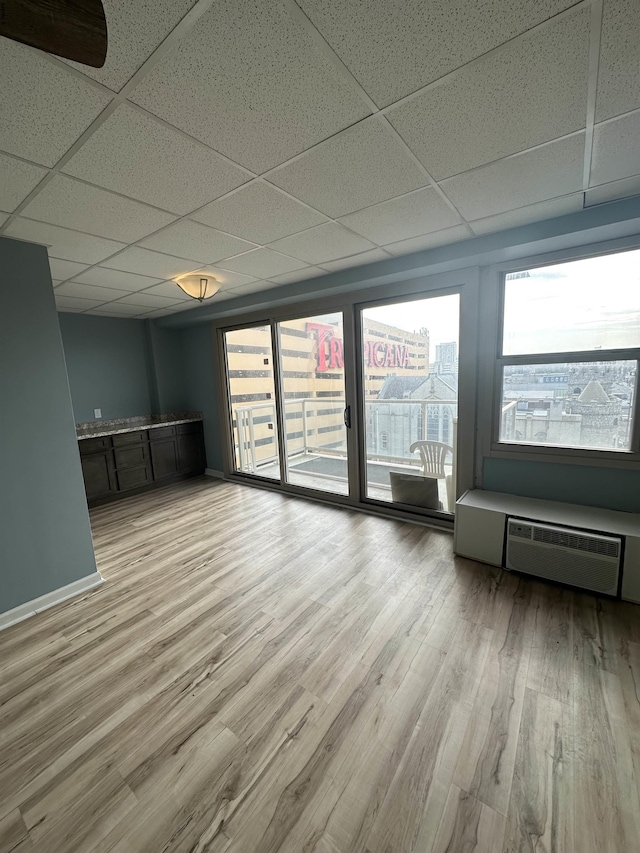 unfurnished living room with a paneled ceiling, healthy amount of natural light, light wood-style flooring, and baseboards