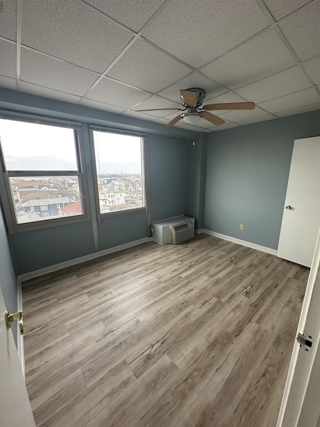 empty room featuring a paneled ceiling, a ceiling fan, wood finished floors, and baseboards