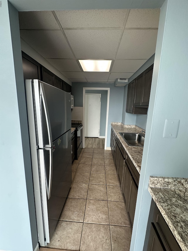 kitchen with a sink, freestanding refrigerator, a paneled ceiling, electric range, and light tile patterned floors