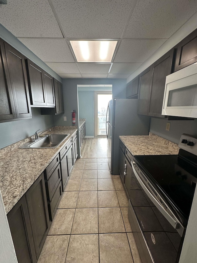 kitchen featuring stainless steel electric range, white microwave, a drop ceiling, a sink, and light countertops