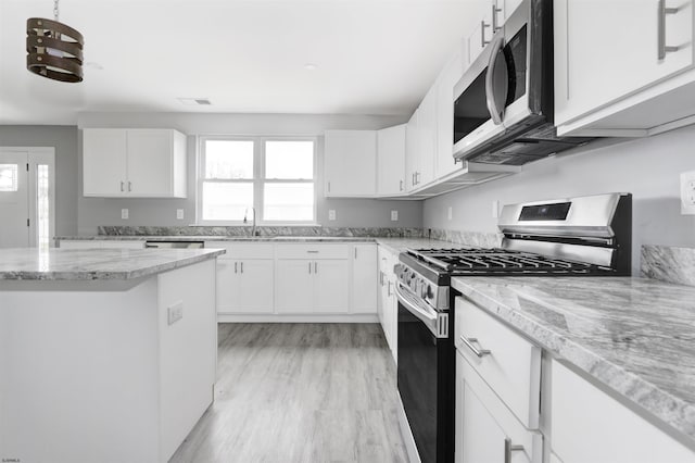 kitchen featuring stainless steel appliances, white cabinetry, light stone countertops, light wood-type flooring, and a sink