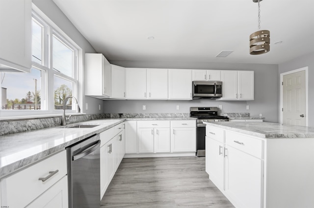 kitchen with appliances with stainless steel finishes, a sink, white cabinetry, light stone countertops, and light wood-style floors