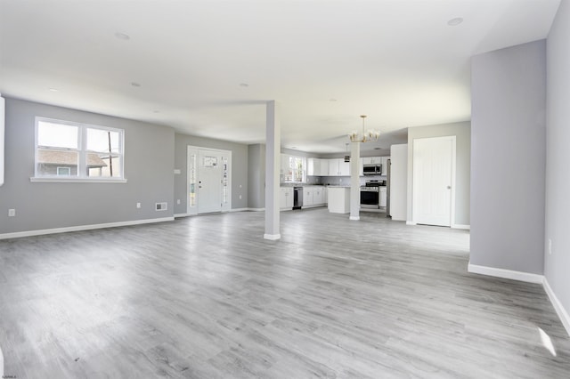 unfurnished living room with a chandelier, baseboards, and light wood-type flooring