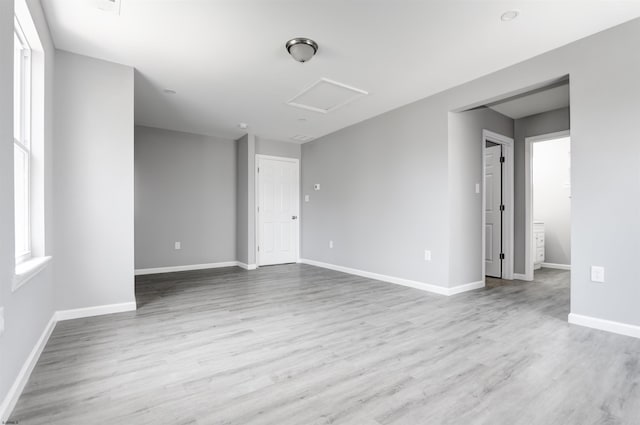empty room featuring attic access, wood finished floors, and baseboards