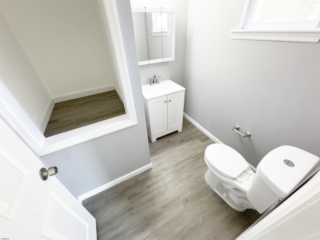 half bath with toilet, wood finished floors, baseboards, and vanity